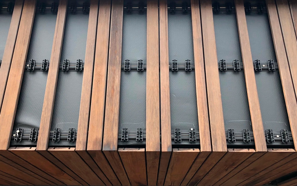 Revestimiento de fachada exterior en madera de bambú formato Varibo con algunas de las lamas extraídas para ver los raíles y los clips
